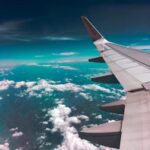 HOME Aerial view of airplane wing over fluffy clouds with a deep turquoise sky.