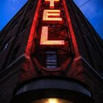 HOME Eye-catching low angle shot of a neon hotel sign illuminating a brick building facade at dusk.
